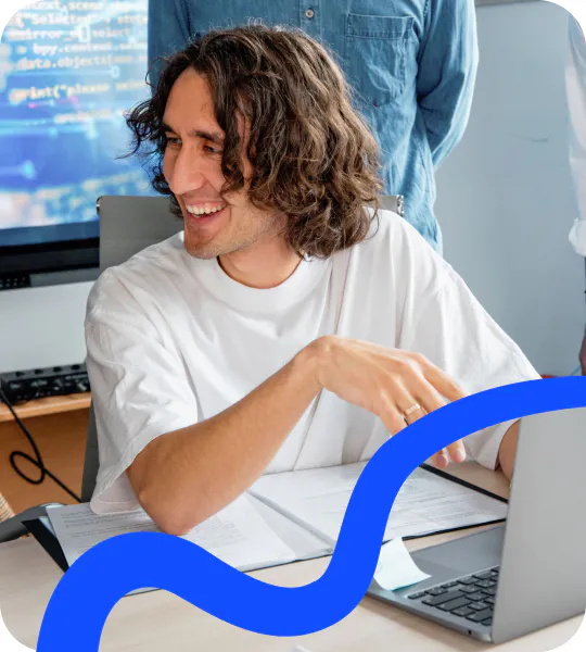 A Flero AI engineer smiling at their laptop while a colleague looks over their shoulder